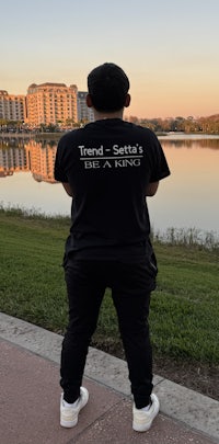 a man standing in front of a lake wearing a black t - shirt